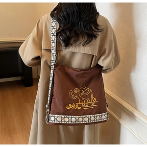 Close-up of brown canvas tote with golden elephant embroidery and geometric strap