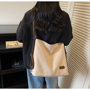 Detail of a large beige canvas tote bag with brown leather straps and reinforced stitching