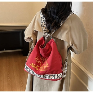 Close-up of red canvas backpack featuring yellow elephant embroidery and woven shoulder strap