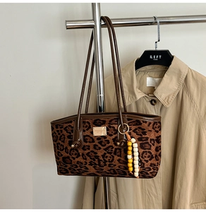 Close-up of leopard print shoulder bag with gold logo and beaded charm on a hanger