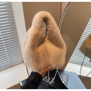Detail of soft plush bucket bag with metal chain strap held by hand in natural light