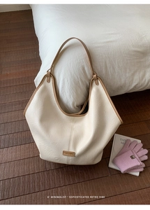 Detailed view of cream leather hobo bag with brown trim and metal logo in home setting