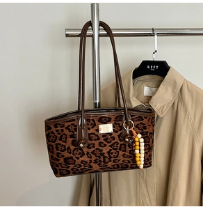 Detail of leopard print tote bag with gold logo plaque and beaded charm accessory