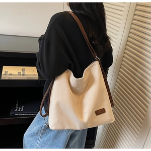 Detail of a large canvas tote bag with brown leather straps and side logo patch