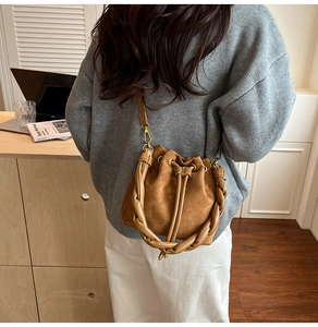 Détail du sac seau en daim marron avec poignée tressée et bandoulière fine