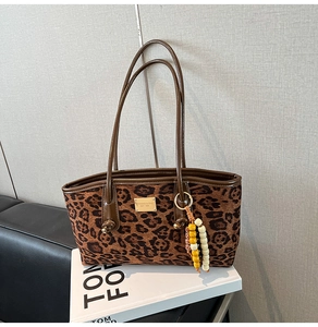 Detail of leopard print tote bag with brown leather handles and decorative beaded pendant