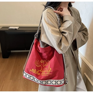 Detail of red canvas bucket bag with yellow elephant embroidery and woven shoulder strap