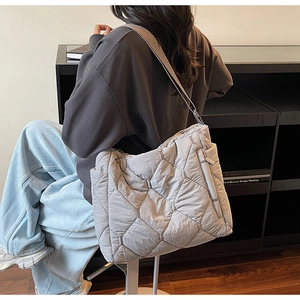 Close-up of the light gray quilted tote bag with wide strap worn as a shoulder bag