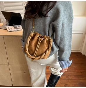 Gros plan du sac seau en daim marron avec une poignée unique en cuir tressé