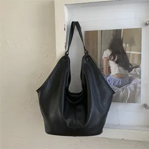 Detail of black pebbled leather Hobo bag with gold logo on a textured beige wall
