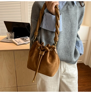 Détail du sac seau en daim marron avec une poignée tressée et une fermeture à cordon
