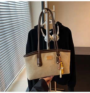 Detail of khaki suede tote bag featuring brown leather trim and retro beaded charm