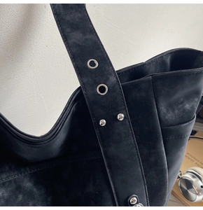 Macro shot of black suede tote bag strap featuring silver eyelets and metal rivets