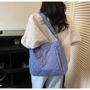 Close-up of a purple quilted tote bag with a wide blue shoulder strap and side zipper
