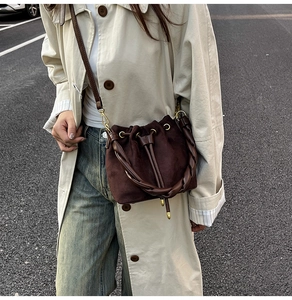 Détail du sac seau en daim marron foncé avec poignée tressée et boucles dorées
