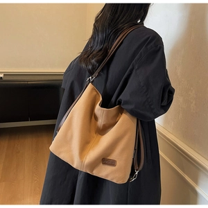 Close-up of camel canvas tote bag with brown straps worn over a dark winter coat