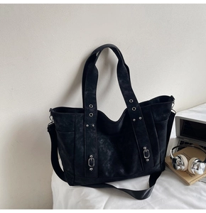 Close-up of black tote bag with silver rivets and side pocket shown in office setting