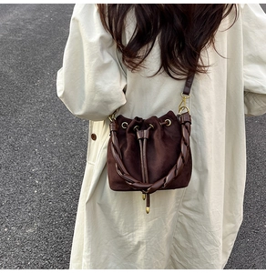 Détail d'un sac seau en daim marron foncé avec poignée en cuir tressé et fermeture à cordon