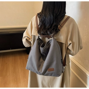 Detail of dark grey canvas tote bag with brown leather straps shown on shoulder