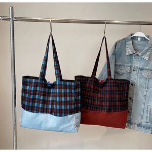 Détail de grands sacs cabas à carreaux bleu et rouge suspendus sur un portant minimaliste