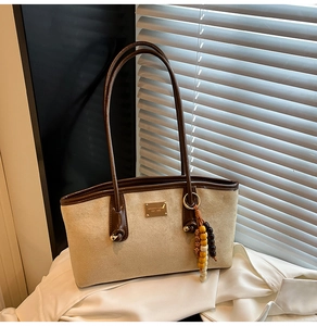 Detail of suede shoulder bag with brown leather trim and retro wooden bead tassel charm