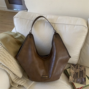 Detail of dark brown hobo bag with leather texture and heart logo on a soft sofa