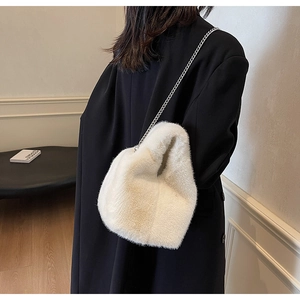 Detail of white faux fur bucket bag with silver chain strap on black wool coat