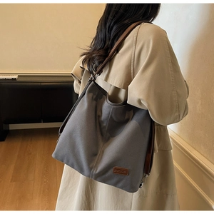 Detail of grey canvas tote bag featuring brown leather straps and branded logo patch
