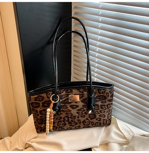 Detail of leopard print tote bag with black leather handles and decorative bead pendant
