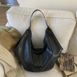 Close-up of a large black leather tote bag featuring a metallic brand logo on a sofa