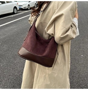 Dettaglio borsa a secchiello in pelle scamosciata bordeaux indossata con trench chiaro