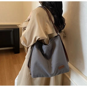 Detail of grey canvas tote bag with brown leather straps and branded logo patch