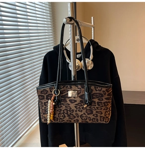 Detail of leopard print tote bag featuring black leather handles and colorful beaded charm