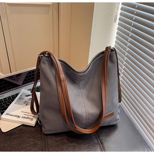 Detailed view of grey canvas tote bag with brown faux leather straps on a dark bench