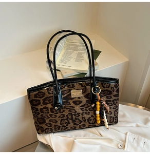Detail of leopard print tote bag featuring a brand metal plate and beaded charm tassel