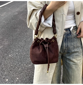 Détail d'un sac seau en daim marron foncé avec poignée torsadée et ferrures dorées