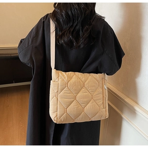 Detailed back view of a beige quilted puffer tote bag worn by a model in a minimalist room