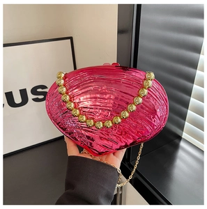 Detail of fuchsia shell-shaped acrylic clutch with gold bead handle and metallic texture