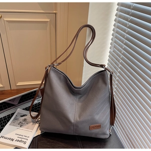 Detail of grey canvas tote bag with brown faux leather trim and brand logo patch