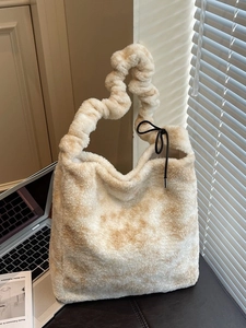 Beige plush tote bag with pleated handle and black drawstring in a modern indoor setting