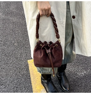 Gros plan d'un sac seau en daim marron foncé avec poignée tressée et détails dorés