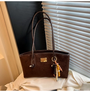 Close-up of deep brown suede tote bag with golden square logo and colorful wood bead charm