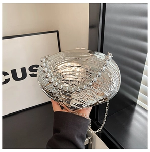 Detail of silver shell-shaped evening clutch with pearl handle and metallic mirror finish