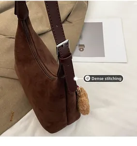 Détail des coutures denses sur le sac cabas en daim marron avec bandoulière et pompon