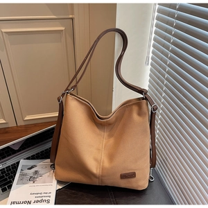 Detail of a large brown canvas tote bag with a leather brand tag in a warm indoor setting