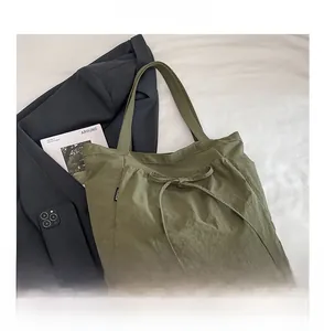 Detail of olive green canvas tote bag featuring drawstring bow and side fashion label