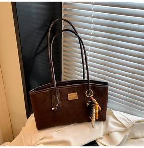 Detail view of brown suede shoulder bag featuring a wood bead tassel and gold metal nameplate
