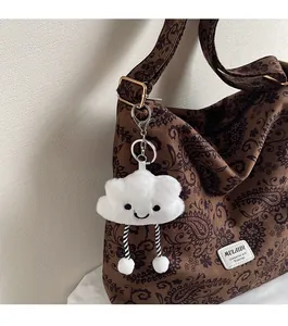 Close-up of a white plush cloud charm with a smiling face on a brown leopard bag