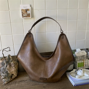 Detail of a large brown hobo bag in textured leather with a metal logo on a wooden desk