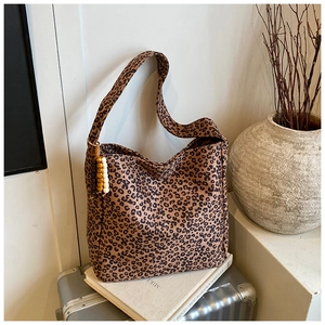 Close-up of leopard print shoulder bag with wooden bead tassel on a travel suitcase
